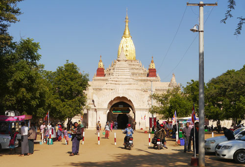Golden spired Burmese temple with cars and motorbikes