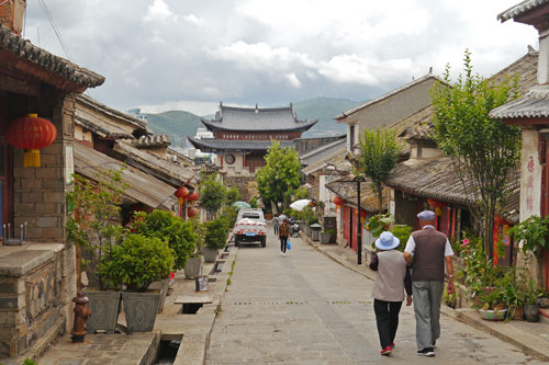 Elderly couple with matching hats walk towards Chinese gatehouse